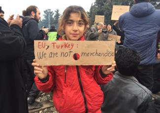 A child from Syria holds a placard reading 'EU, Turkey: We are not merchandise' at a camp for refugees and migrants at a camp in Idomeni, Northern Greece.